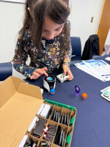 A young girl peers at a Vex device as she taps the top of it.