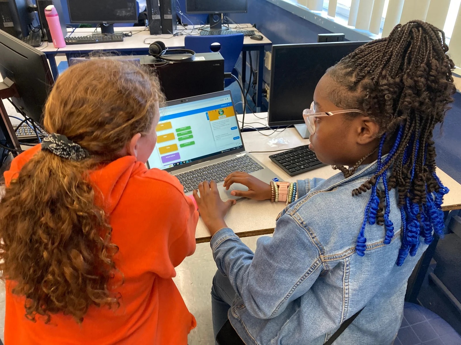 2 young students code at a laptop in a computer lab